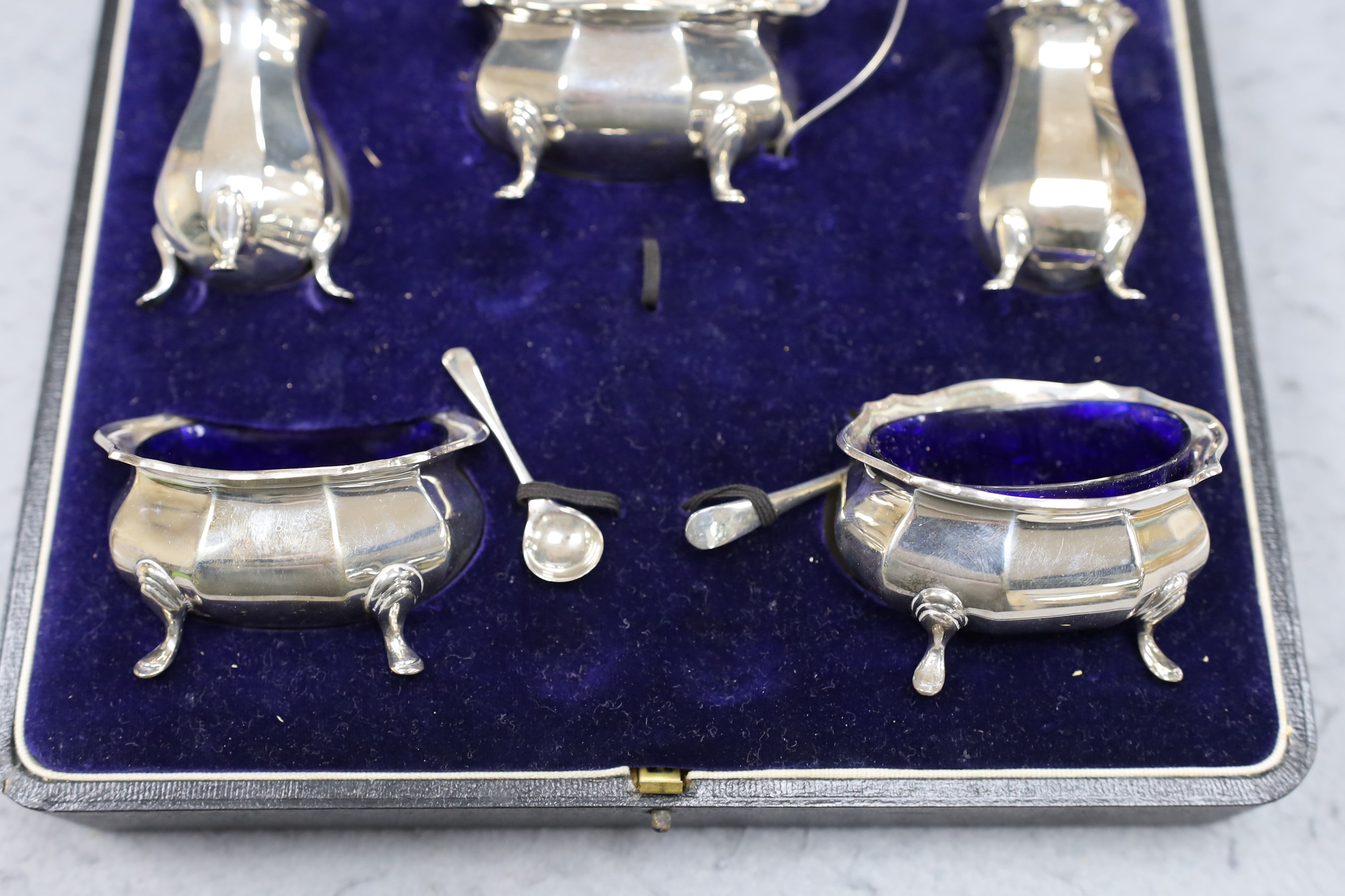 A cased George V silver five piece condiment set, Birmingham, 1921, with two associated spoons, one silver and one plated.